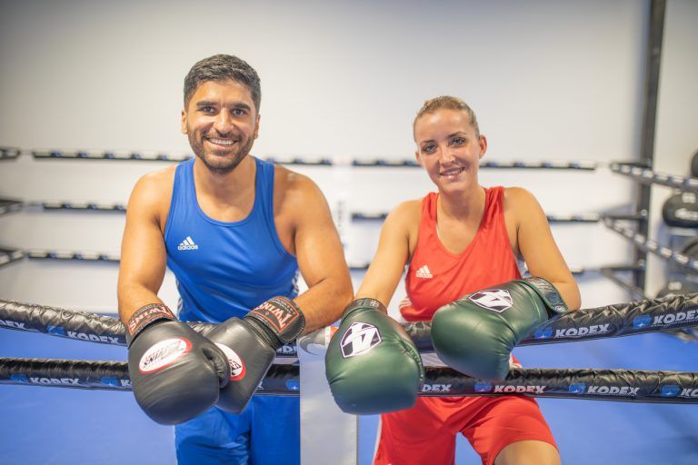 Unsere Boxtrainer Laura und Dilan hängen bequem über unseren Boxring und zeigen ihr schönstes Lächeln